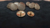 12 round metal buttons in gold and black. They have an embossed design and a shank on the back. Six buttons are larger, and six are smaller. These buttons can be used for coats, blazers, suits, sherwanis, and other Indian dresses. 
